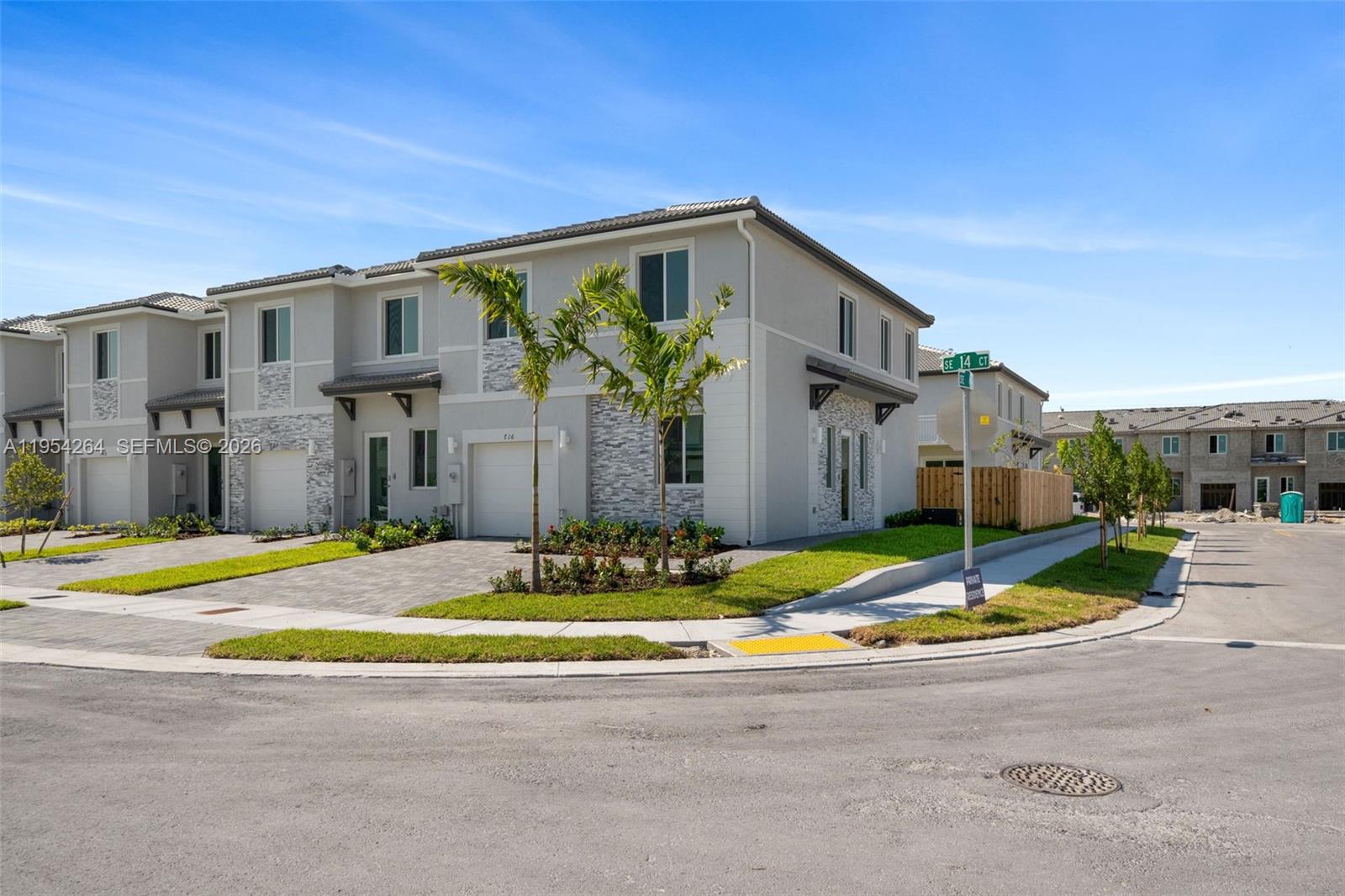 A two-story townhouse with a stone-accented facade, paved driveway, and palm trees on a corner — 716 SE 14th Ct, Homestead FL 33034, HOMESTEAD, FL