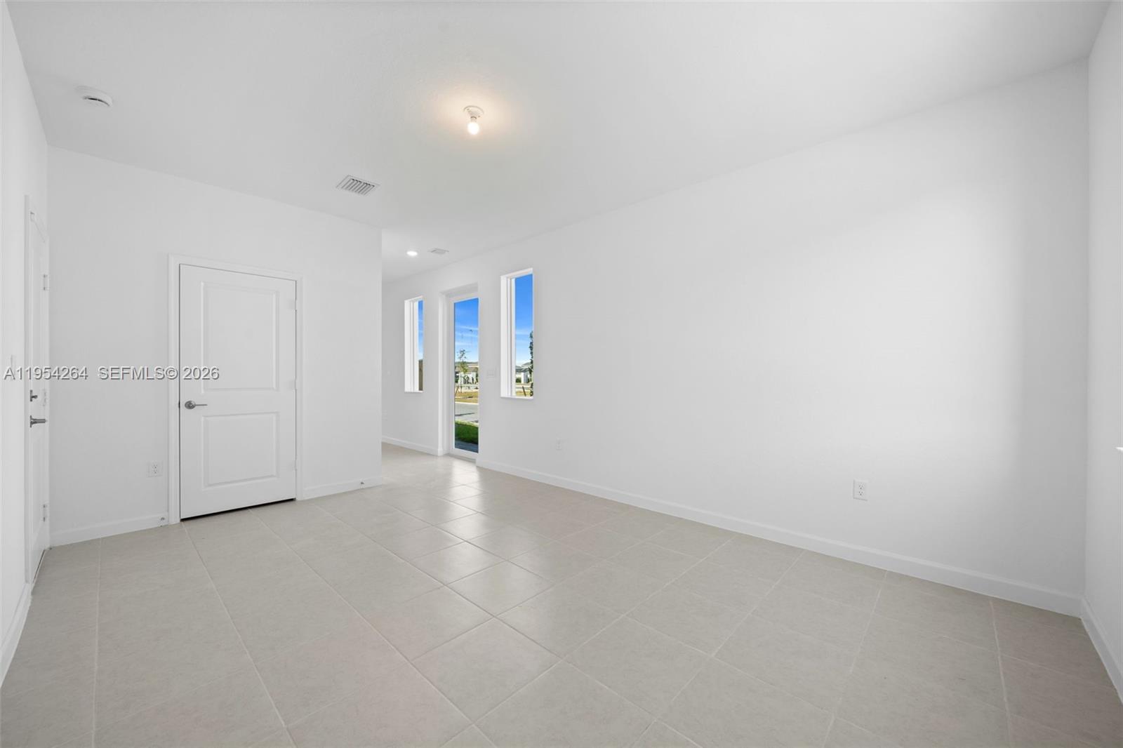 An empty room features white walls, light-colored tile flooring, and a glass door to outside — 716 SE 14th Ct, Homestead FL 33034, HOMESTEAD, FL