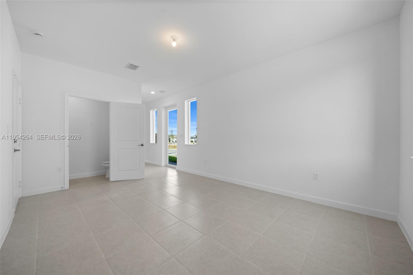 An empty room with white walls, light tile flooring, and an attached bathroom — 716 SE 14th Ct, Homestead FL 33034, HOMESTEAD, FL