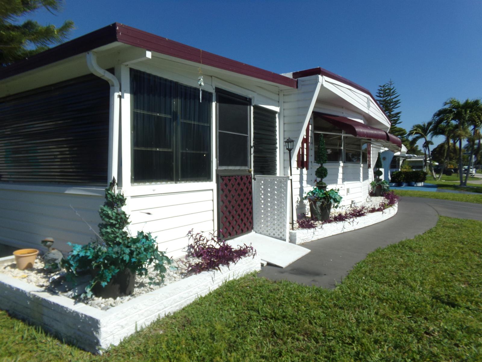 A white mobile home with a maroon roof, screen door, and landscaped brick planter beds — 6385 Cypress Lane, Atlantis FL 33462, ATLANTIS, FL