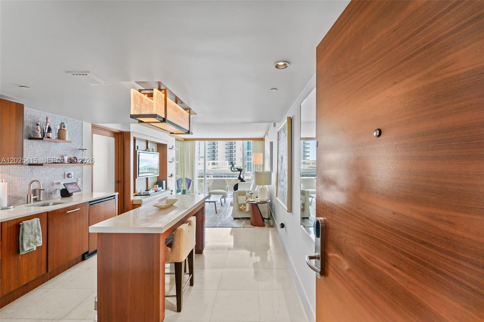 A modern kitchen with wood cabinetry and a breakfast bar opens into a living area — 6801 Collins Ave # 708, Miami Beach FL 33141, MIAMI BEACH, FL