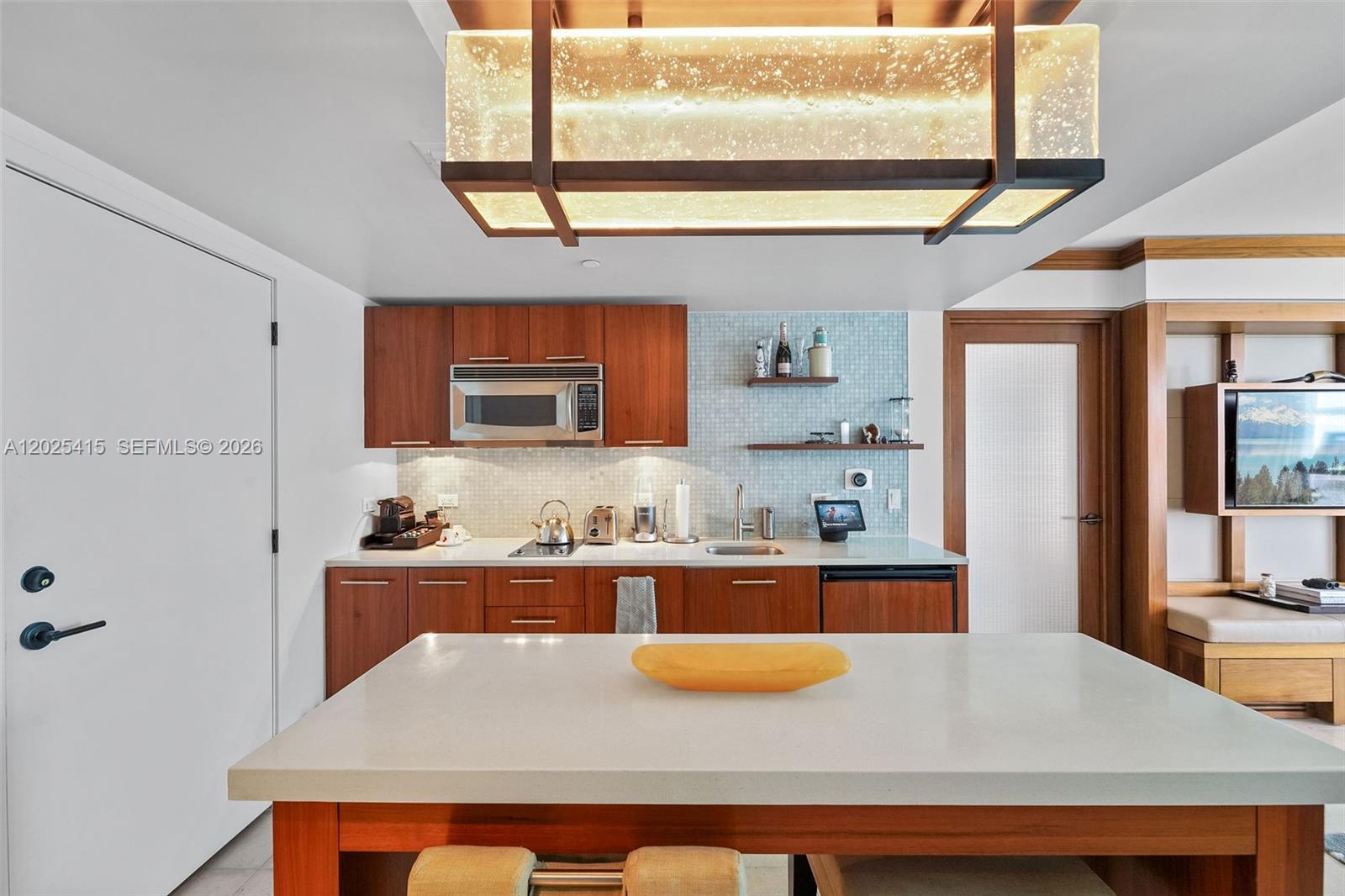 A kitchen features wood cabinetry, a white island, and a rectangular light fixture above — 6801 Collins Ave # 708, Miami Beach FL 33141, MIAMI BEACH, FL