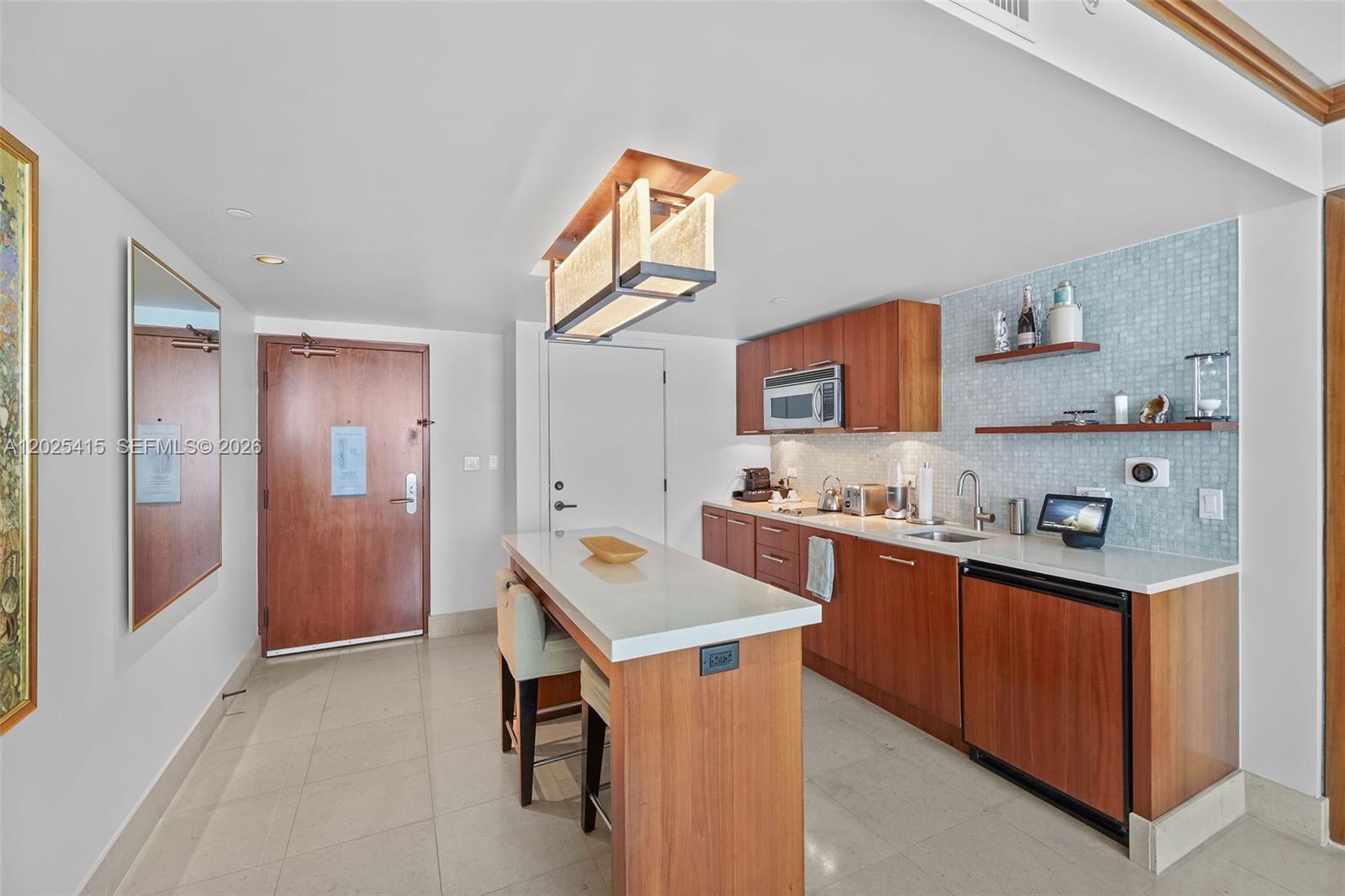 A kitchen features wood cabinets, a white countertop island, and a light blue tiled backsplash — 6801 Collins Ave # 708, Miami Beach FL 33141, MIAMI BEACH, FL