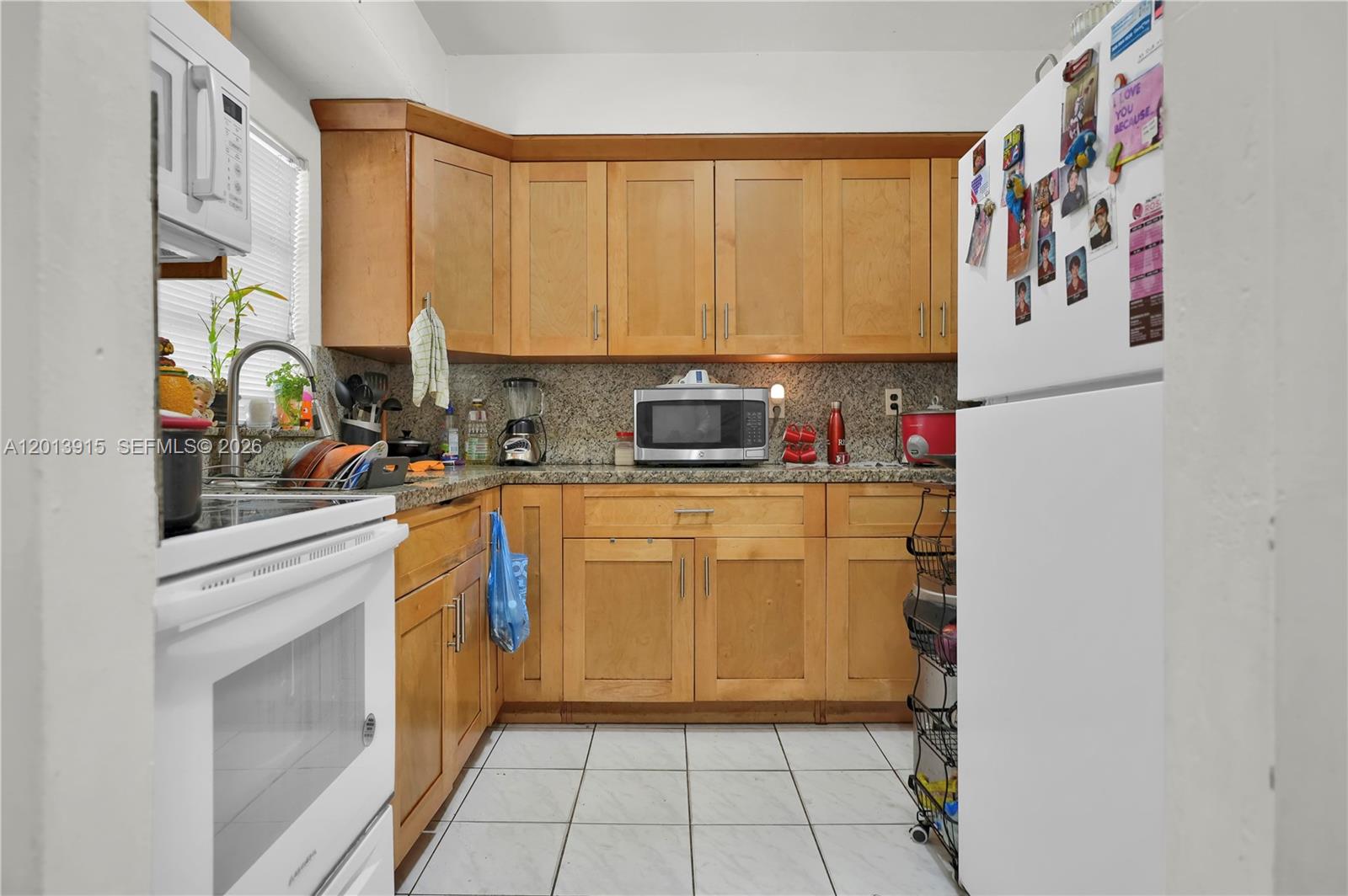 A kitchen features light wood cabinets, granite countertops, white appliances, and white tiled flooring — 201 NW 25th Ave, Miami FL 33125, MIAMI, FL