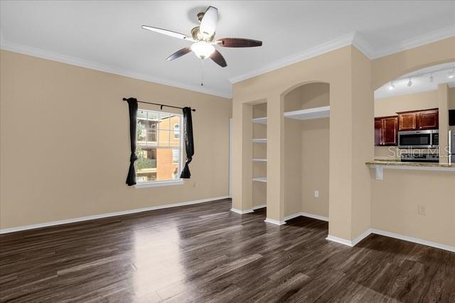 A living room with wood-look flooring, a ceiling fan, built-in shelving, and an adjacent kitchen — 246 VILLA DI ESTE TERRACE UNIT 200, LAKE MARY, FL