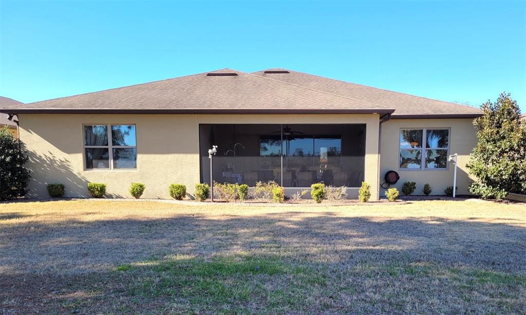 The rear exterior of a tan house features a screened-in patio and a grassy yard — 6443 SW 97TH TERRACE ROAD, OCALA, FL