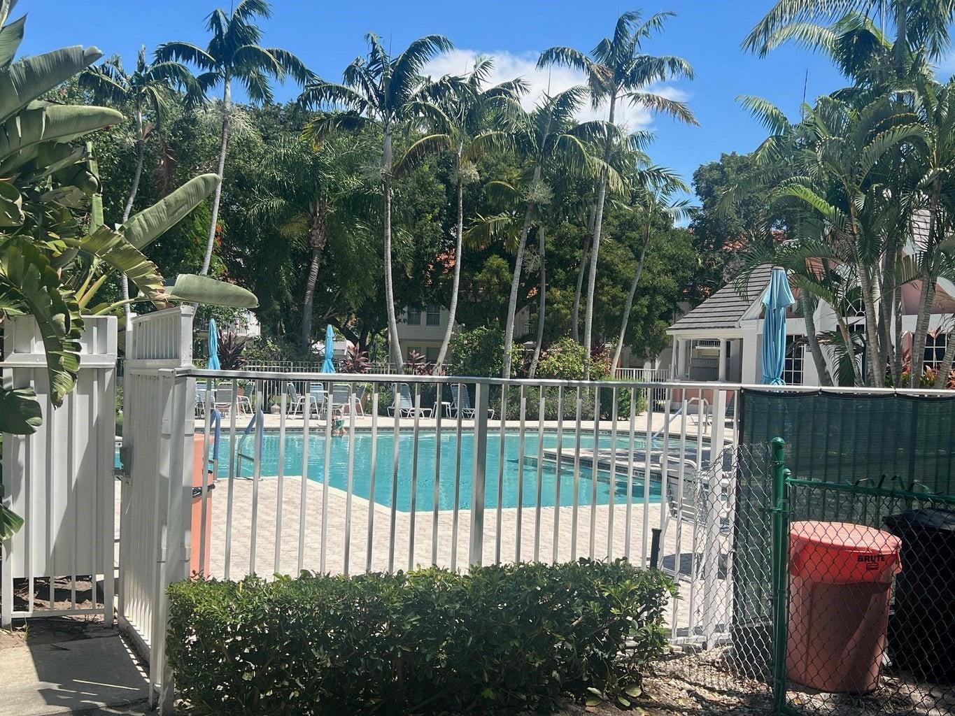 A swimming pool surrounded by a metal fence, palm trees, and a small building — 1050 Crystal Way # D, Delray Beach FL 33444, DELRAY BEACH, FL