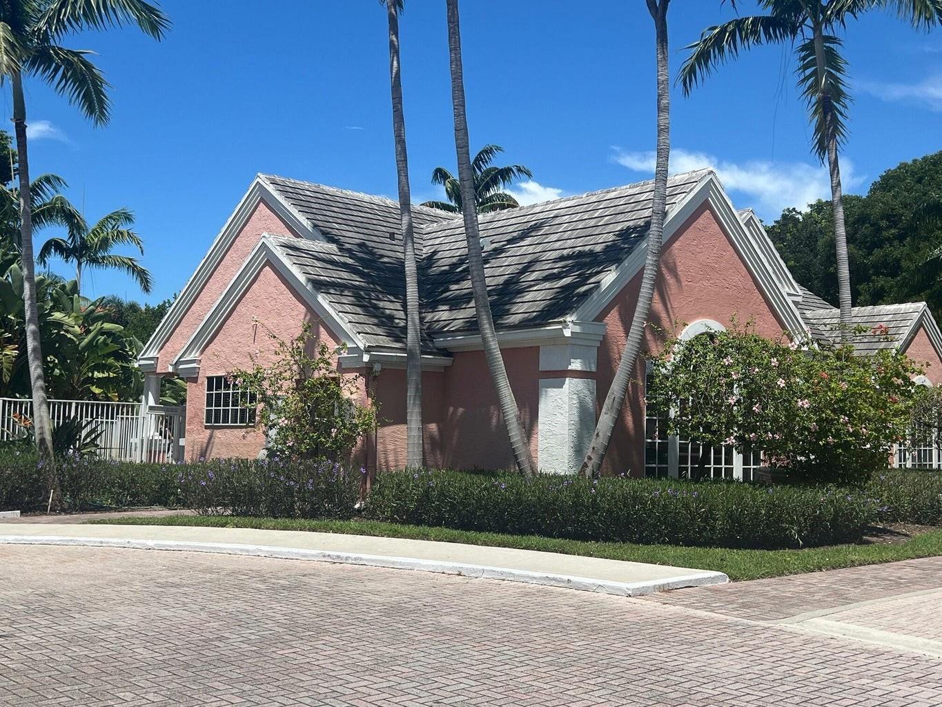 A pink stucco building with a gray tiled roof sits behind a manicured hedge — 1050 Crystal Way # D, Delray Beach FL 33444, DELRAY BEACH, FL