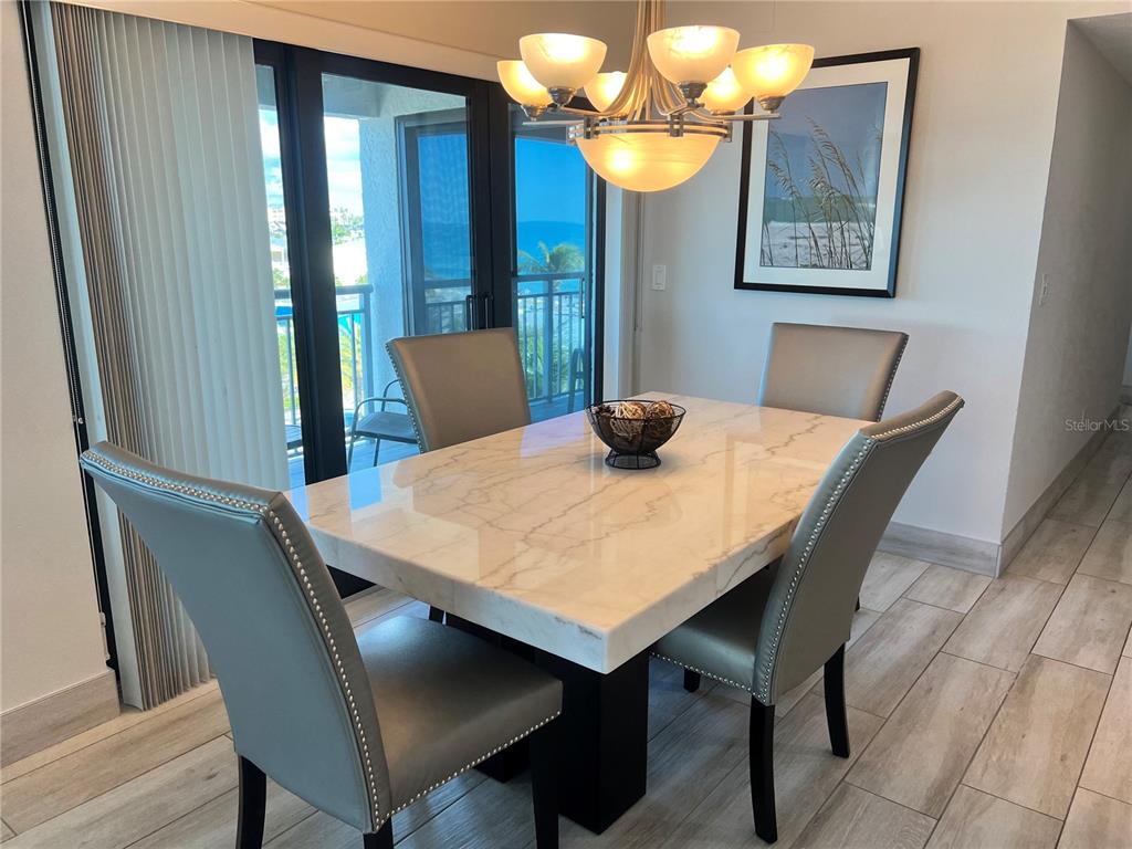 A dining room features a marble-topped table, four upholstered chairs, and a view of the ocean — 1001 POINT OF ROCKS ROAD UNIT 512, SARASOTA, FL