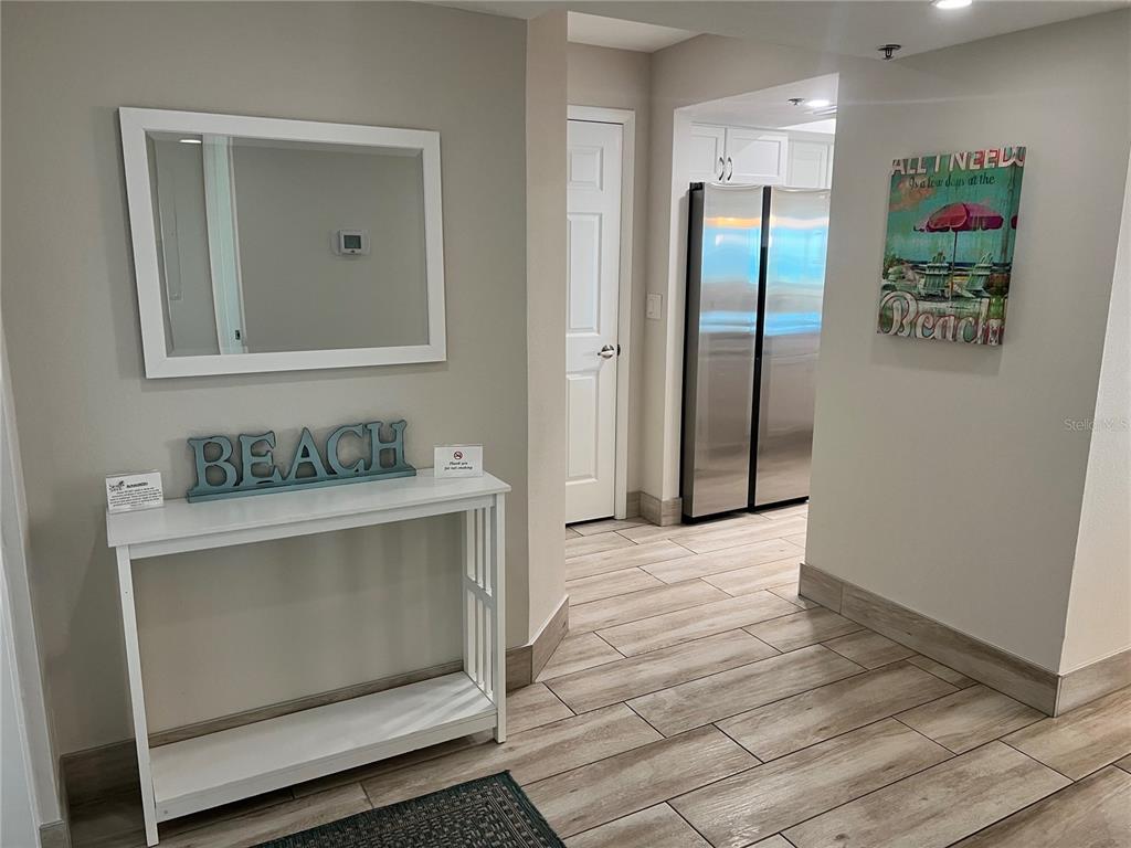 A hallway features wood-look tile flooring, a white console table, a mirror, and beach-themed decor — 1001 POINT OF ROCKS ROAD UNIT 512, SARASOTA, FL