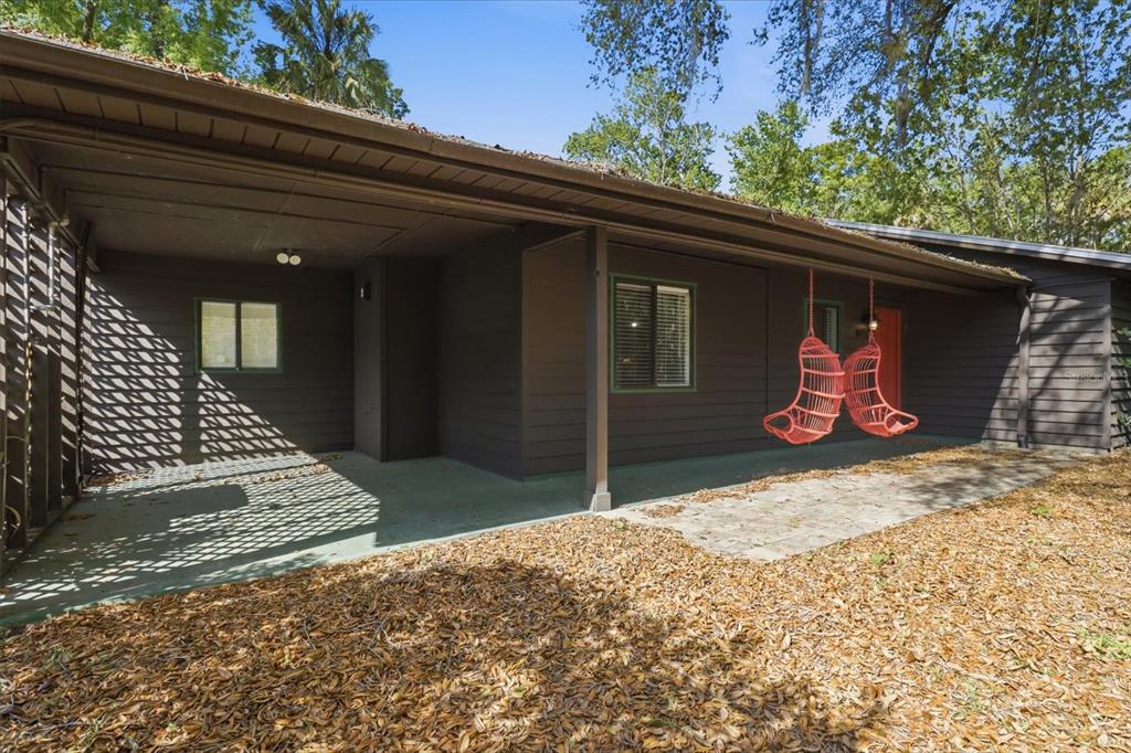 A brown house exterior features a covered patio with two hanging orange chairs and lattice — 8952 W WHITE DOGWOOD DRIVE, HOMOSASSA, FL