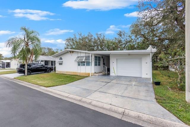 A white single-story manufactured home features a concrete driveway, a carport, and a palm tree — 34124 ESTATES LANE, WESLEY CHAPEL, FL