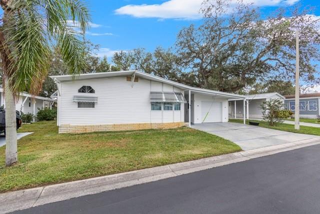 A single-story white mobile home with a carport and a small front lawn — 34124 ESTATES LANE, WESLEY CHAPEL, FL