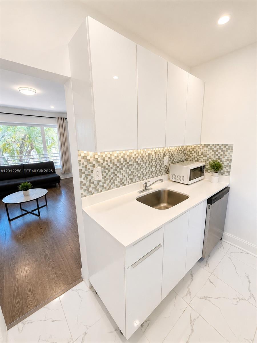 A small kitchen features white cabinets, a stainless steel sink, and a mosaic tile backsplash — 1540 Jefferson Ave # 2, Miami Beach FL 33139, MIAMI BEACH, FL