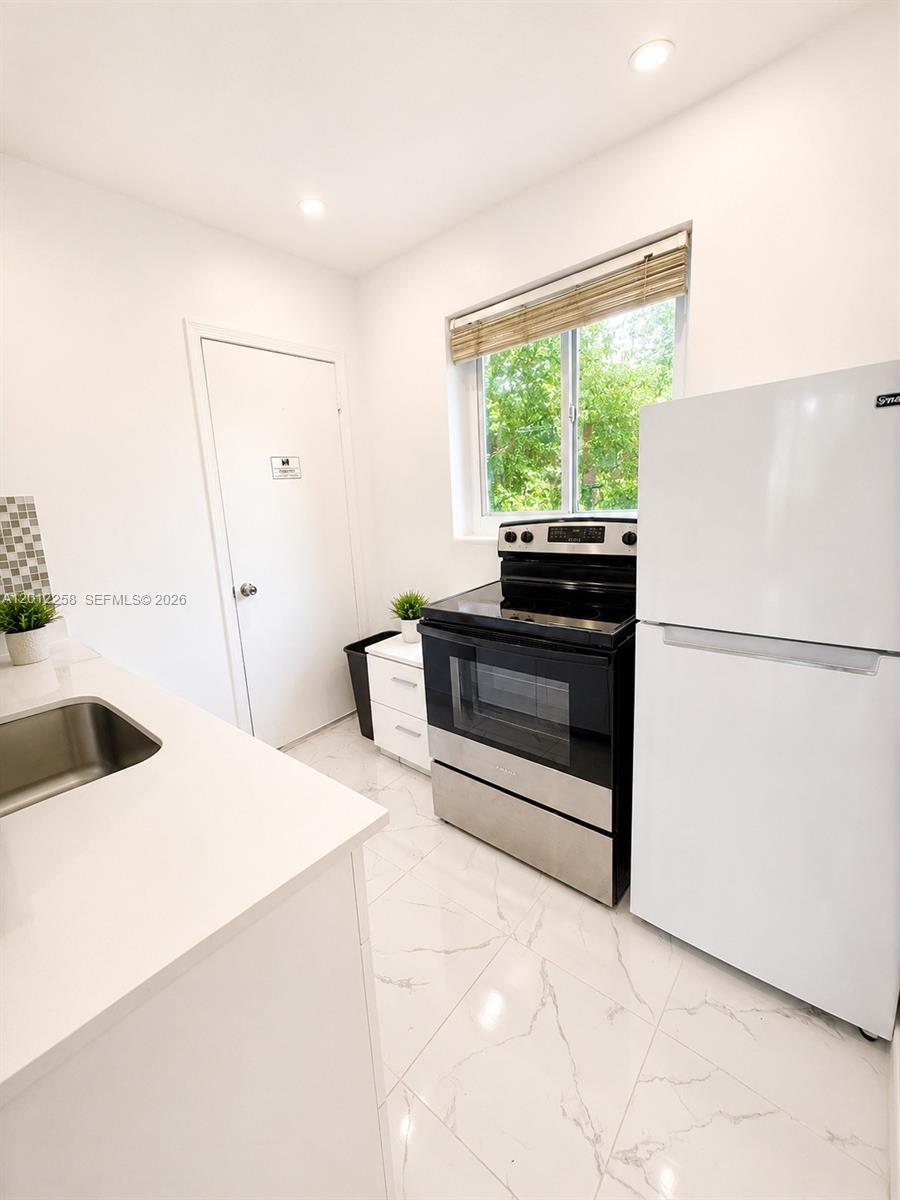 A white kitchen features a stainless steel stove, white refrigerator, and marble-patterned tile flooring — 1540 Jefferson Ave # 2, Miami Beach FL 33139, MIAMI BEACH, FL