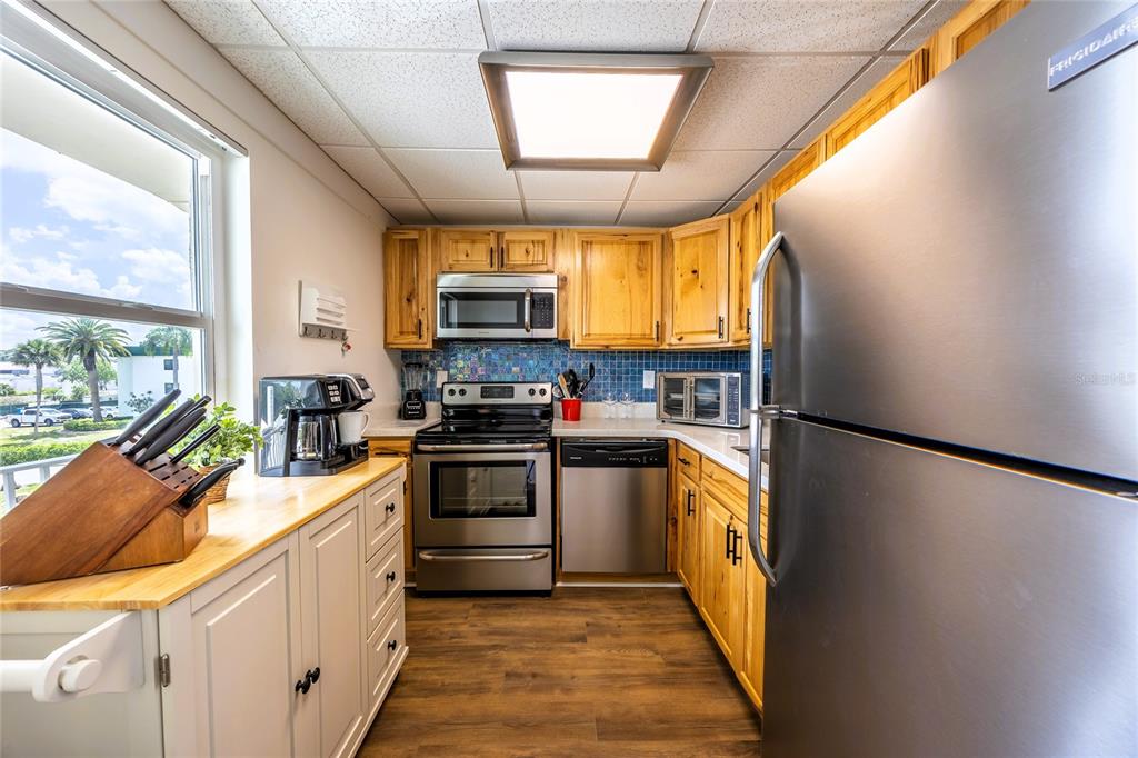 A kitchen features wood cabinets, stainless steel appliances, a blue tile backsplash, and wood flooring — 6220 AUGUSTA DRIVE UNIT 309, FORT MYERS, FL