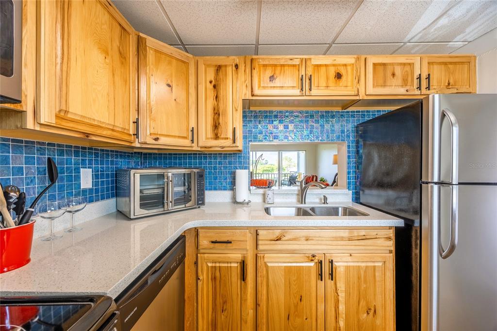 A kitchen features knotty wood cabinets, blue tile backsplash, stainless appliances, and white countertops — 6220 AUGUSTA DRIVE UNIT 309, FORT MYERS, FL