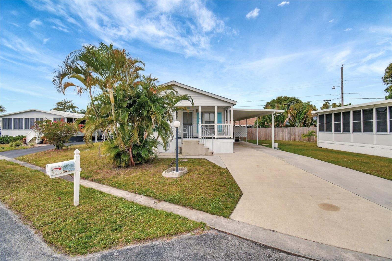 A single-story manufactured home with a palm tree, a concrete driveway, and a covered porch — 14567 Sunset Drive, Delray Beach FL 33445, DELRAY BEACH, FL