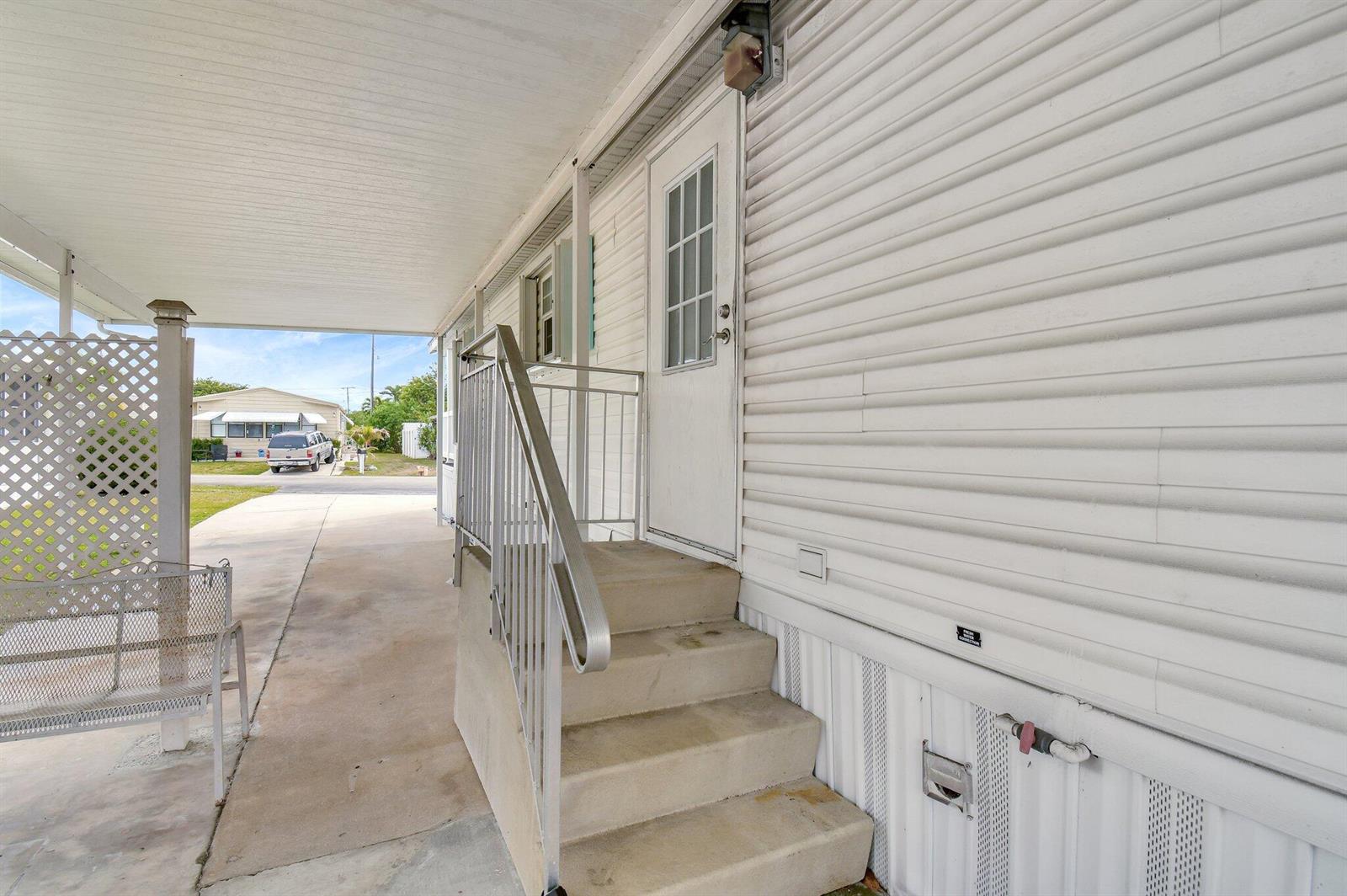 A white mobile home exterior features concrete steps with a metal railing and a carport — 14567 Sunset Drive, Delray Beach FL 33445, DELRAY BEACH, FL