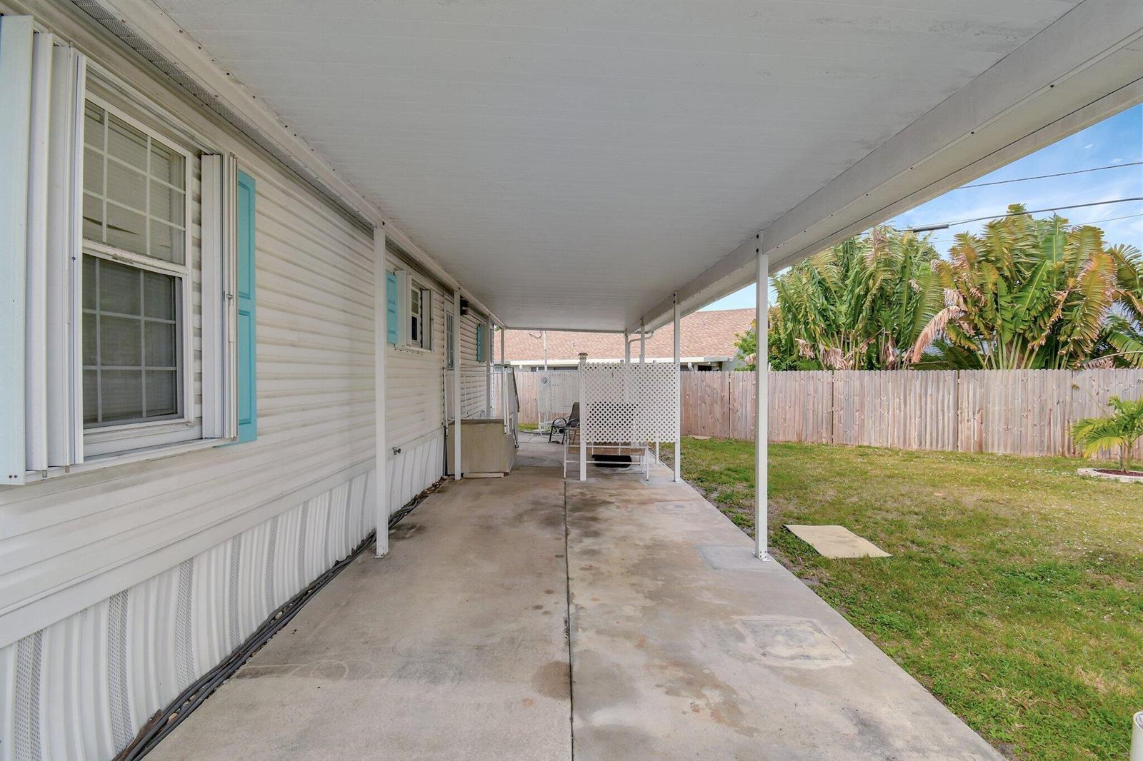 A covered concrete patio runs along the side of a mobile home with a fenced yard — 14567 Sunset Drive, Delray Beach FL 33445, DELRAY BEACH, FL