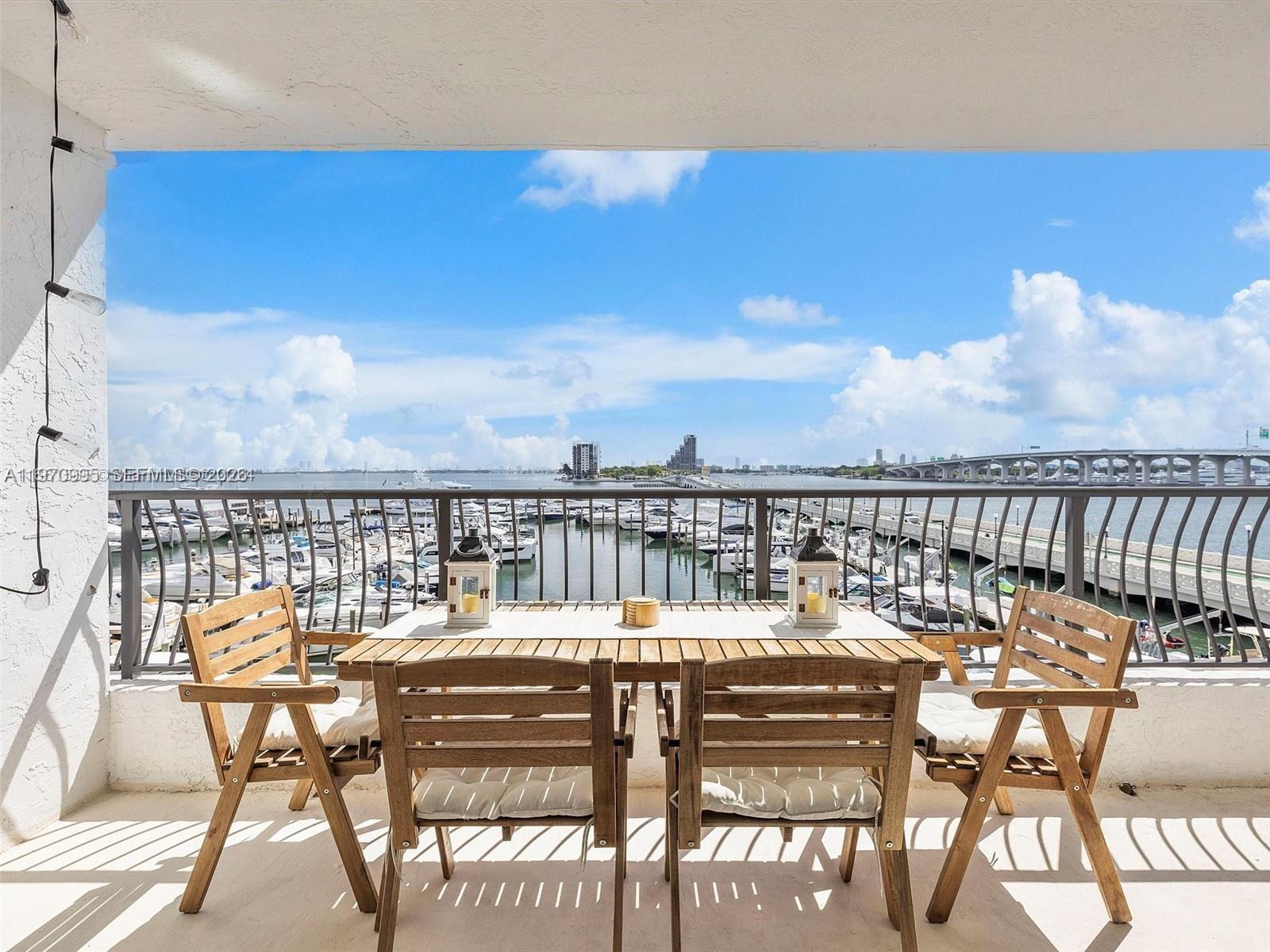 A balcony features a wooden dining set overlooking a marina and a bridge — 555 NE 15th St # 408, Miami FL 33132, MIAMI, FL