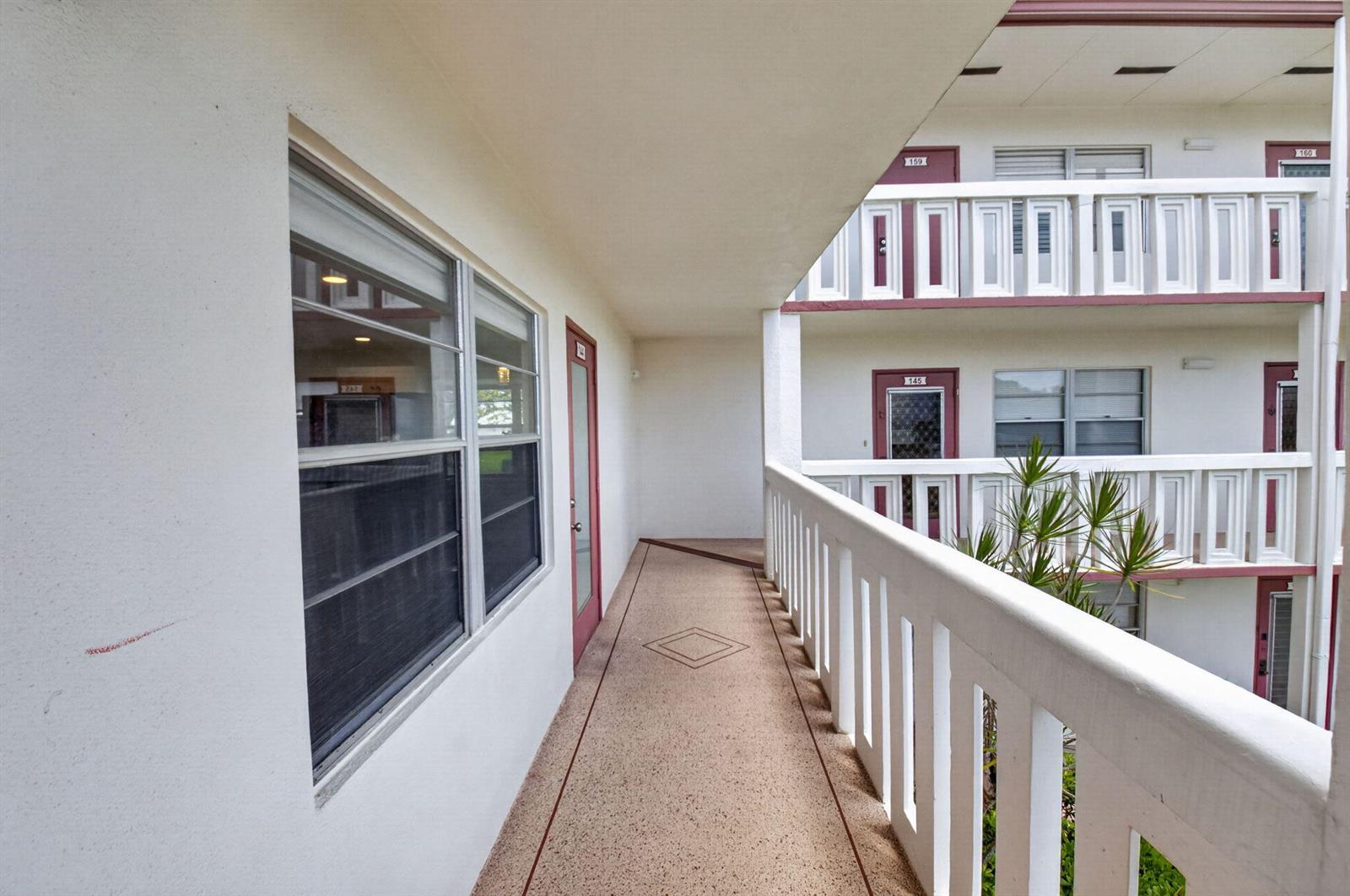 An outdoor walkway features a textured floor, white railings, and several apartment doors — 144 Fanshaw D, Boca Raton FL 33434, BOCA RATON, FL