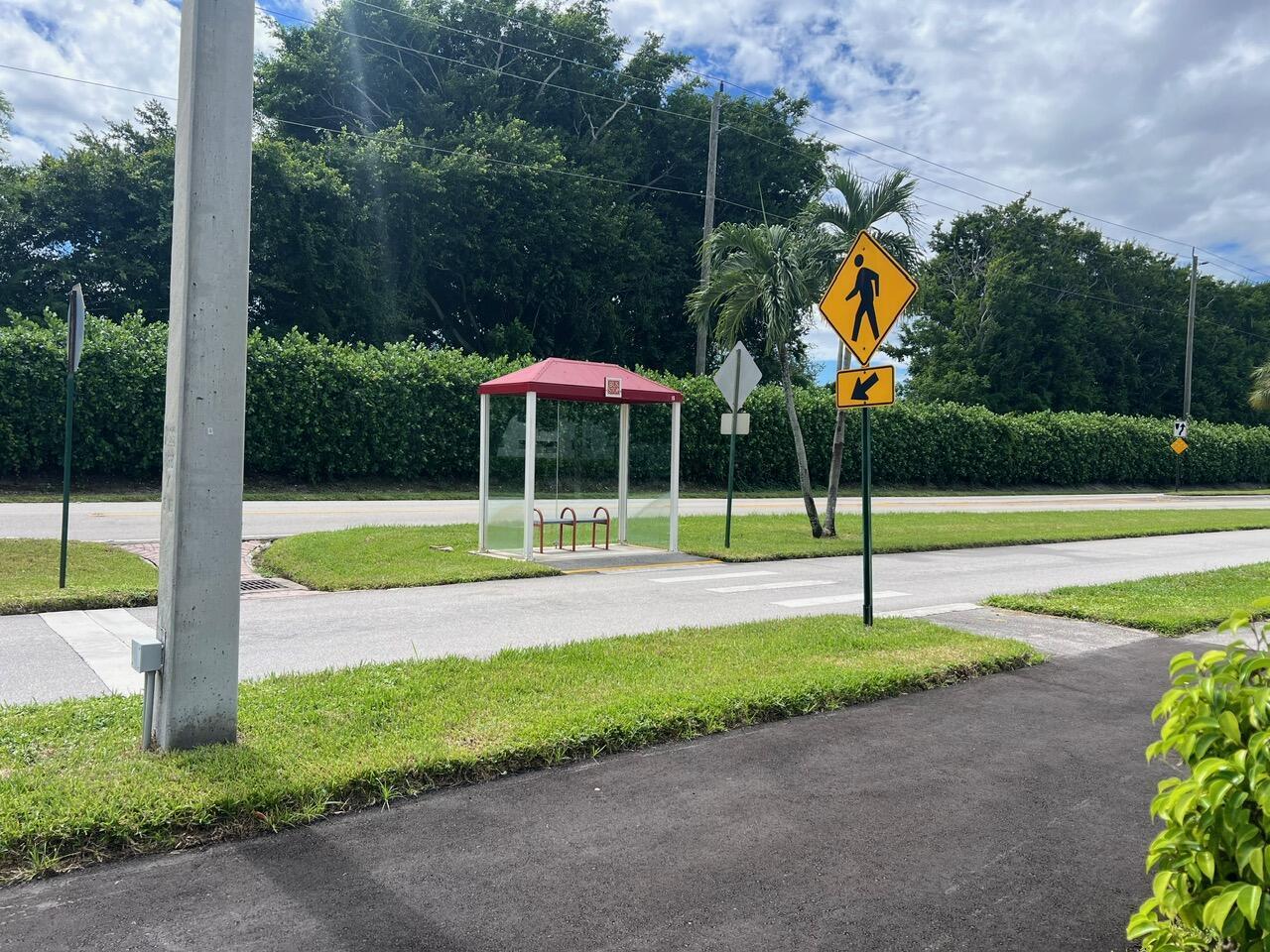 A bus stop shelter sits on a grassy roadside next to a pedestrian crossing sign — 144 Fanshaw D, Boca Raton FL 33434, BOCA RATON, FL