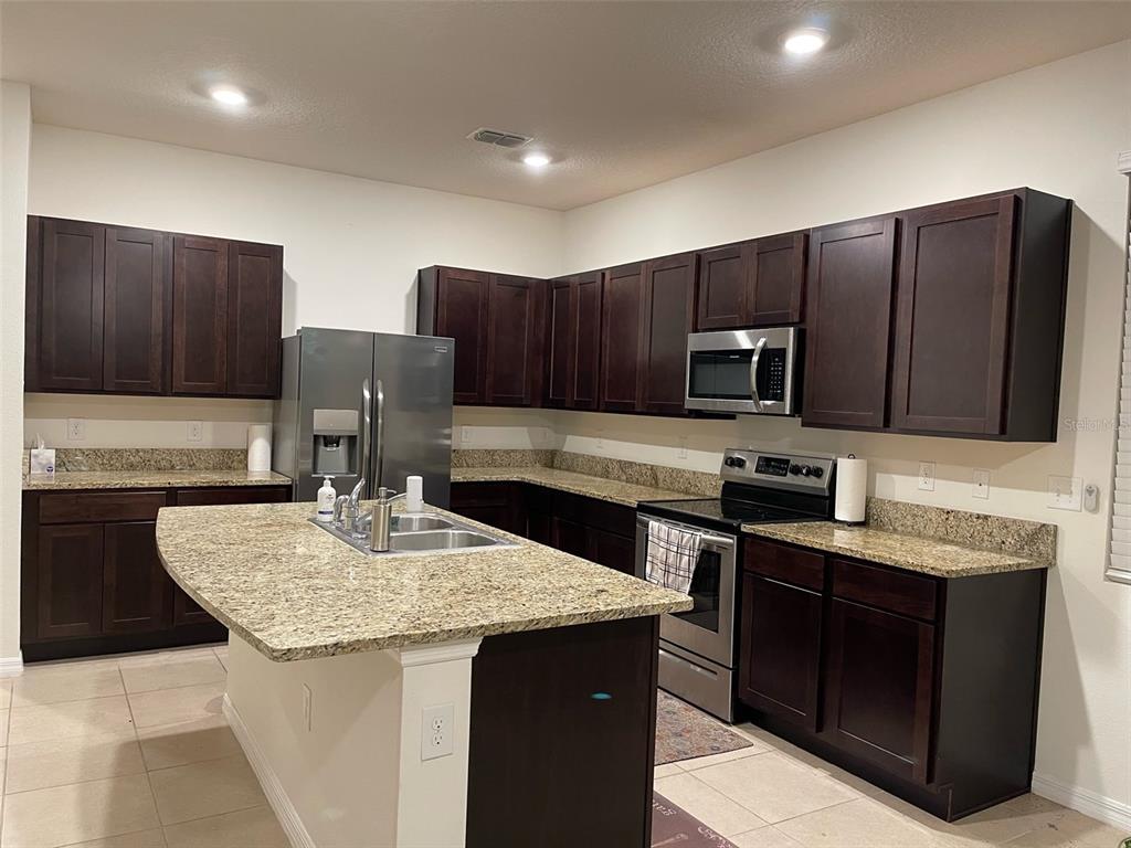 A kitchen features dark wood cabinets, granite countertops, stainless steel appliances, and a central island — 3244 PLEASANT WILLOW COURT, BRANDON, FL