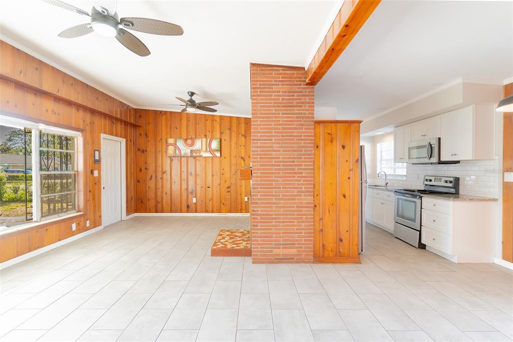A room with wood-paneled walls, a brick fireplace column, and an adjacent white kitchen — 495 AVENUE F SE, WINTER HAVEN, FL