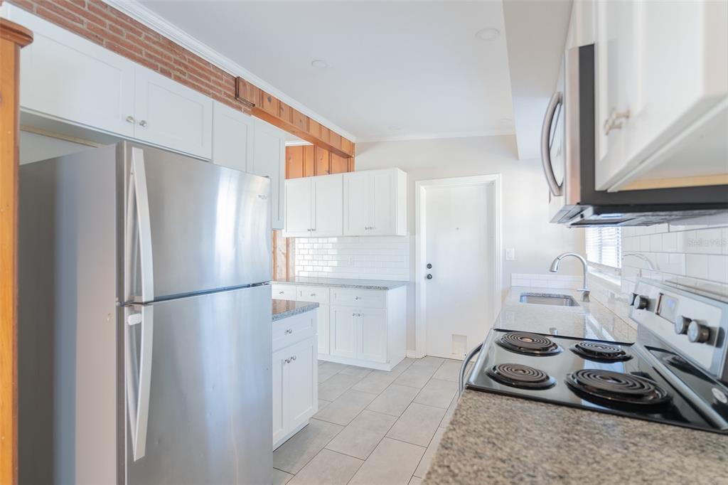 A kitchen features white cabinets, stainless steel appliances, granite countertops, and an exposed brick wall — 495 AVENUE F SE, WINTER HAVEN, FL
