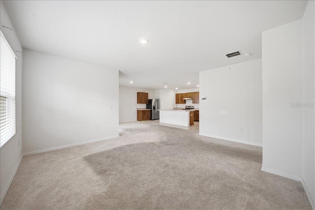 An open-concept living area with beige carpeting leads to a kitchen with wooden cabinets — 750 LAFAYETTE LANE, HAINES CITY, FL