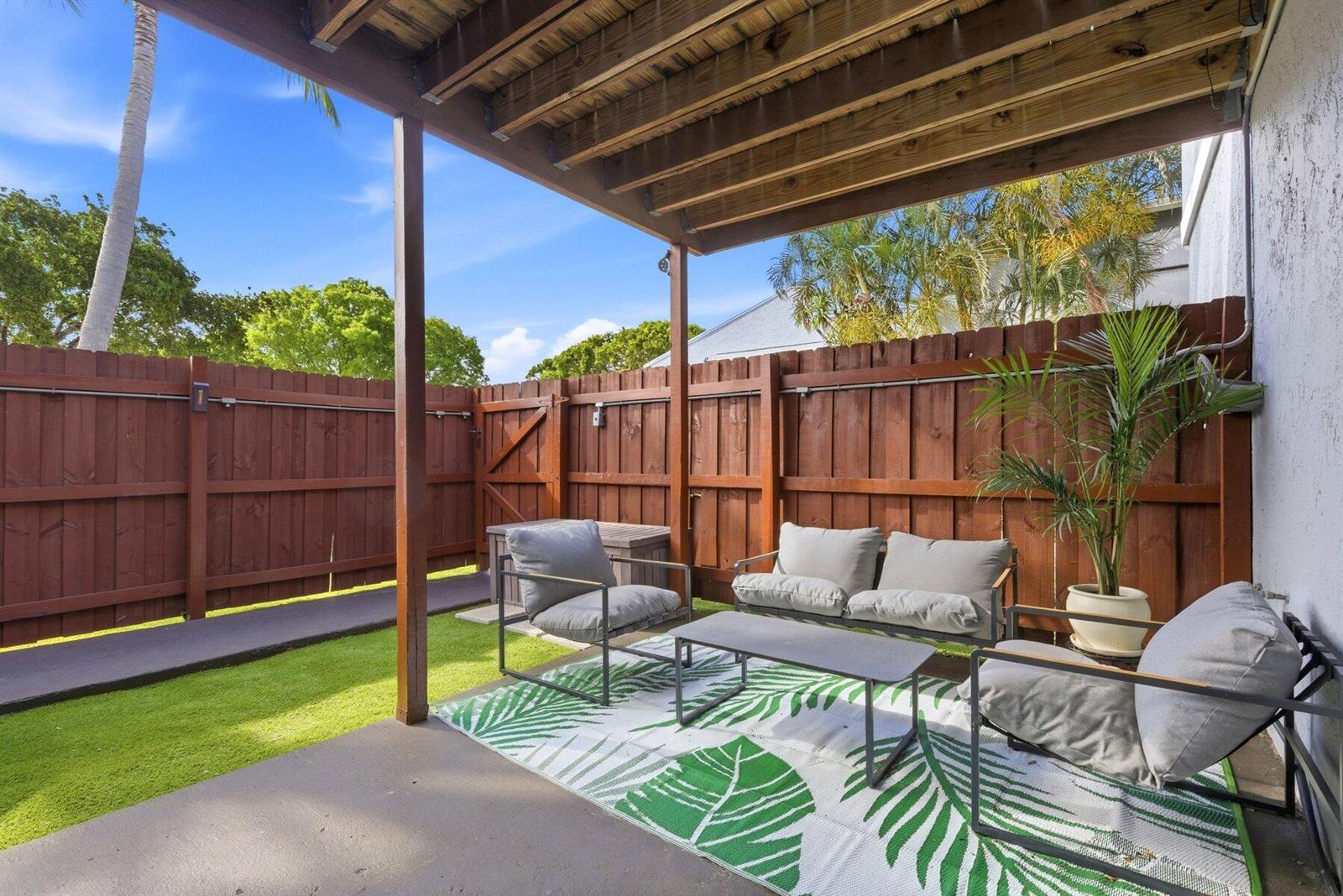 A covered patio features a seating area with a rug, chairs, and a wooden fence — 30 Crossings Circle # G, Boynton Beach FL 33435, BOYNTON BEACH, FL