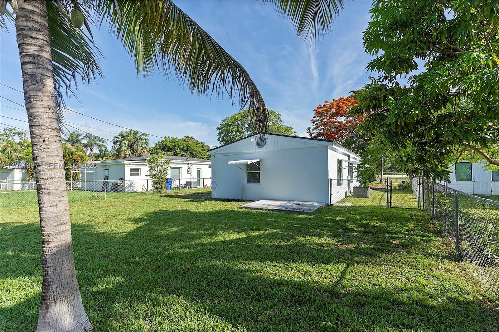 A white house with a concrete patio sits in a grassy backyard with palm trees — 2024 NE 174th St, North Miami Beach FL 33162, NORTH MIAMI BEACH, FL