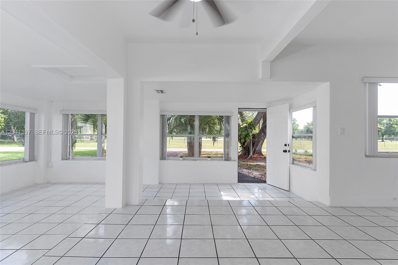 A bright, white-walled room features tiled floors, a ceiling fan, and multiple windows — 2024 NE 174th St, North Miami Beach FL 33162, NORTH MIAMI BEACH, FL