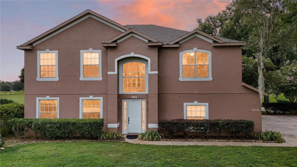A two-story brown stucco house features a central arched entryway and multiple grid-patterned windows — 7314 SPRING MOUNTAIN LANE, YALAHA, FL