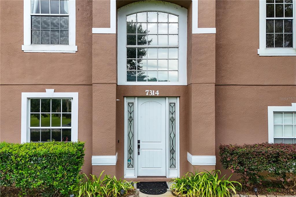 The exterior of a two-story house features a white front door with sidelights and windows — 7314 SPRING MOUNTAIN LANE, YALAHA, FL