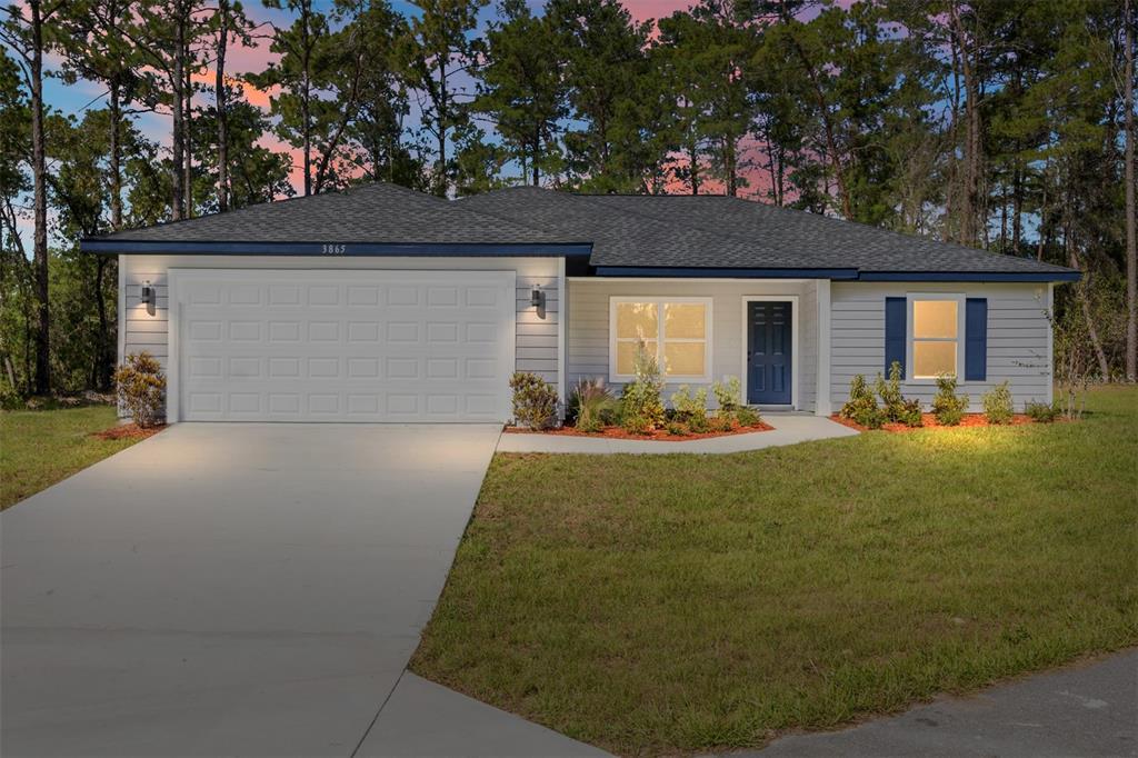A single-story house with gray siding, a white garage door, and a surrounding wooded area — 24303 SW SAILBOAT DRIVE, DUNNELLON, FL