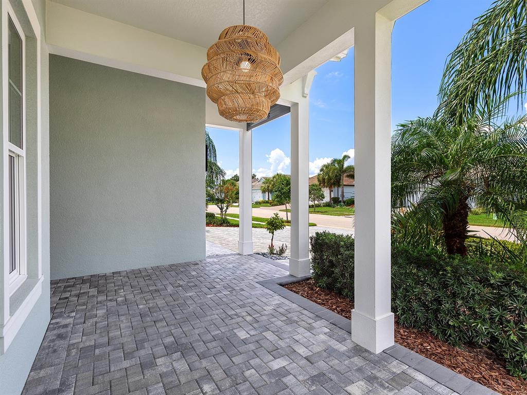 A covered front porch with gray paver flooring, white columns, and a woven pendant light — 8282 GRANDE SHORES DRIVE, SARASOTA, FL
