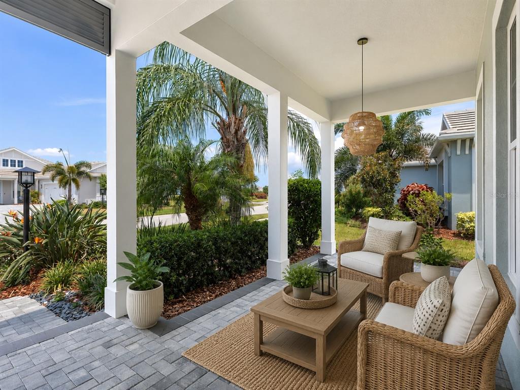 A covered patio features wicker chairs, a wooden coffee table, and views of tropical landscaping — 8282 GRANDE SHORES DRIVE, SARASOTA, FL