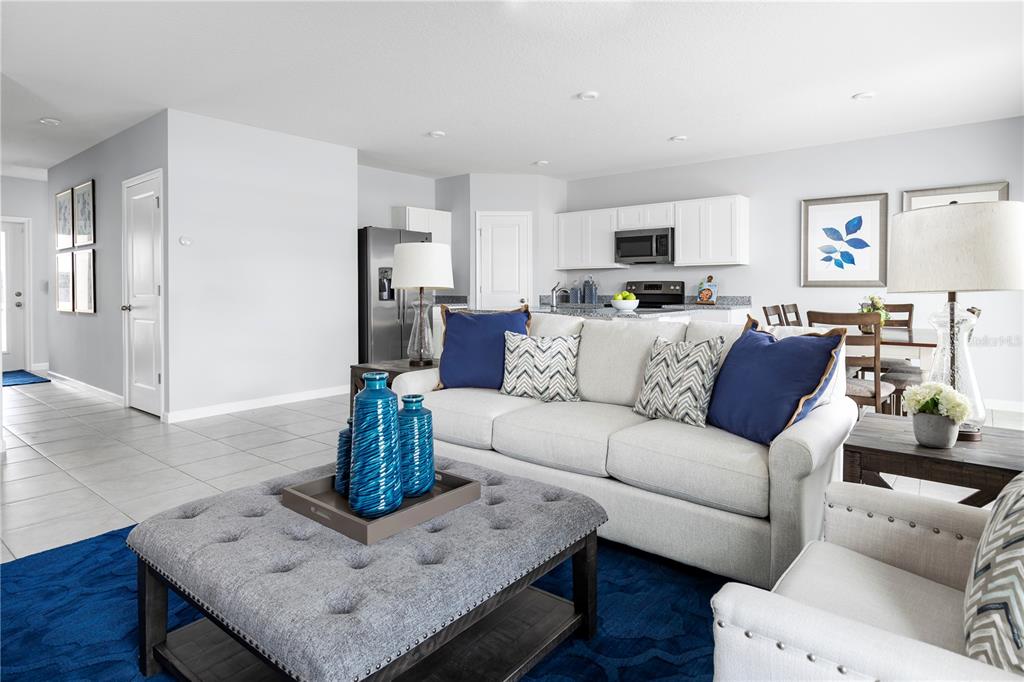A living room features a grey tufted ottoman, a light-colored sofa, and an open kitchen — 7682 SE 114TH STREET, BELLEVIEW, FL