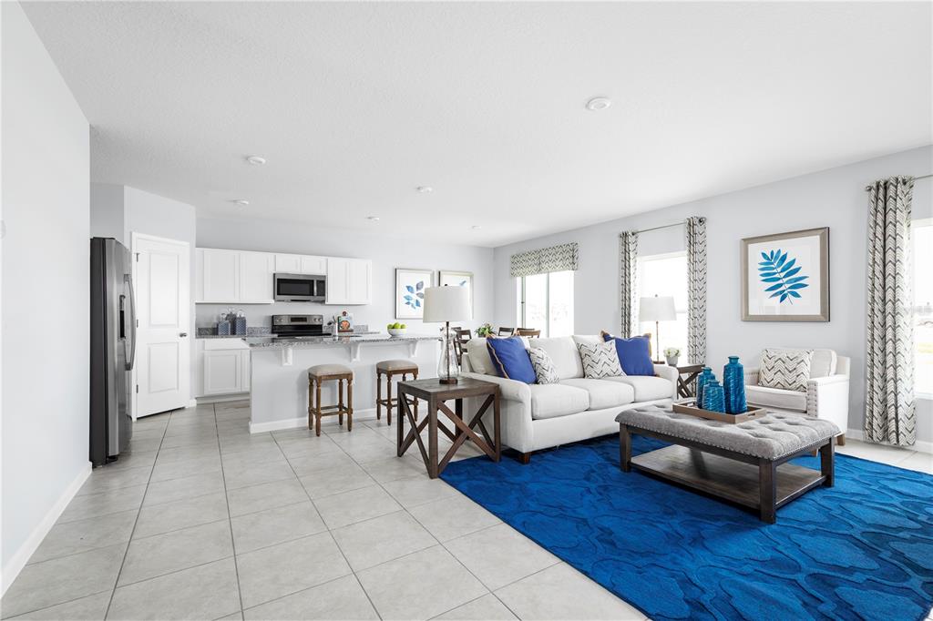 An open-concept living room and kitchen featuring white cabinetry, tile flooring, and a blue rug — 7682 SE 114TH STREET, BELLEVIEW, FL