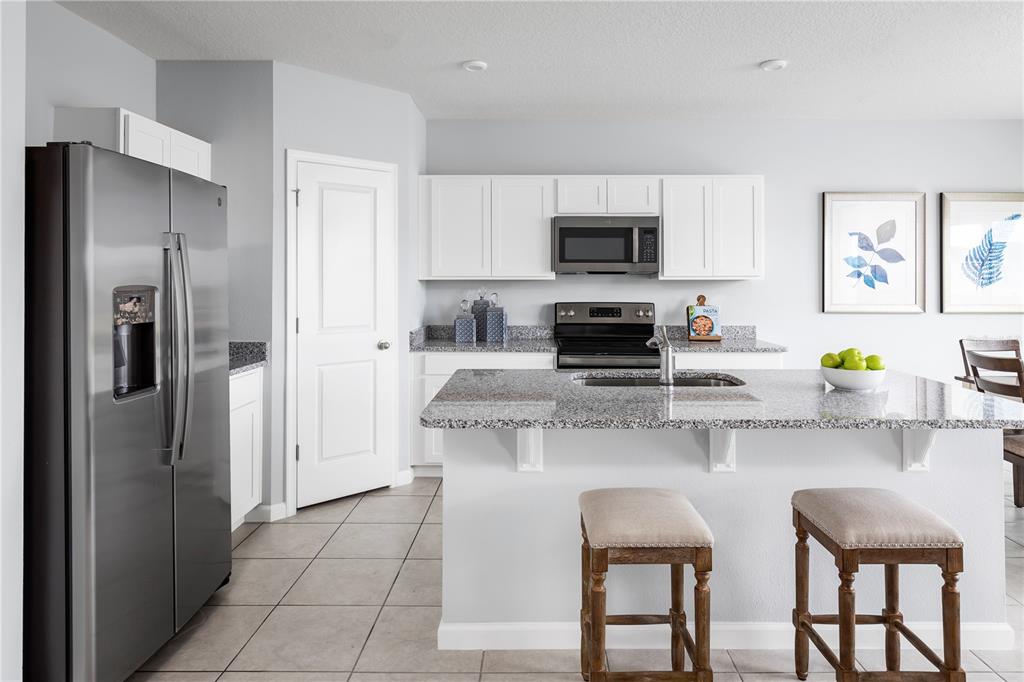 A kitchen features white cabinets, granite countertops, a stainless steel refrigerator, and a breakfast island — 7682 SE 114TH STREET, BELLEVIEW, FL