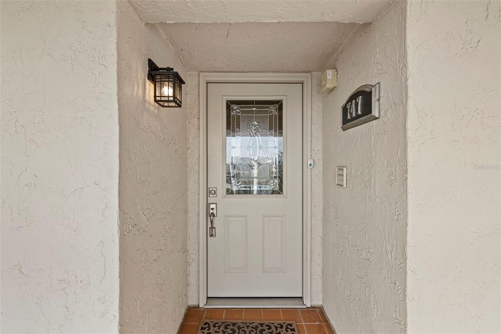 A white front door with a decorative glass insert sits in a recessed entryway — 8150 BRENT STREET UNIT 747, PORT RICHEY, FL