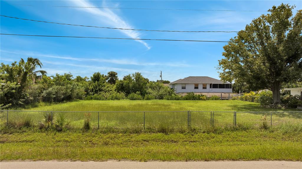 A fenced, grassy vacant lot sits in front of a house under a blue sky — 321 POMPANO TERRACE, PUNTA GORDA, FL