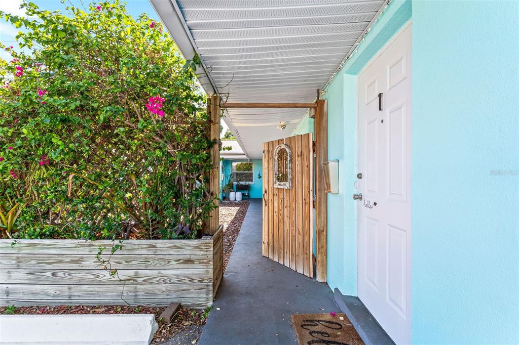 A light blue building exterior features a wooden gate, a white door, and lush landscaping — 1230 70TH STREET N, ST PETERSBURG, FL