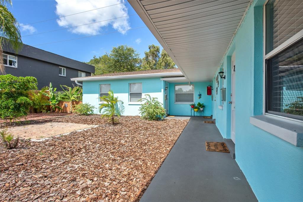 A light blue exterior wall features a covered walkway, windows, and a wood chip yard — 1230 70TH STREET N, ST PETERSBURG, FL