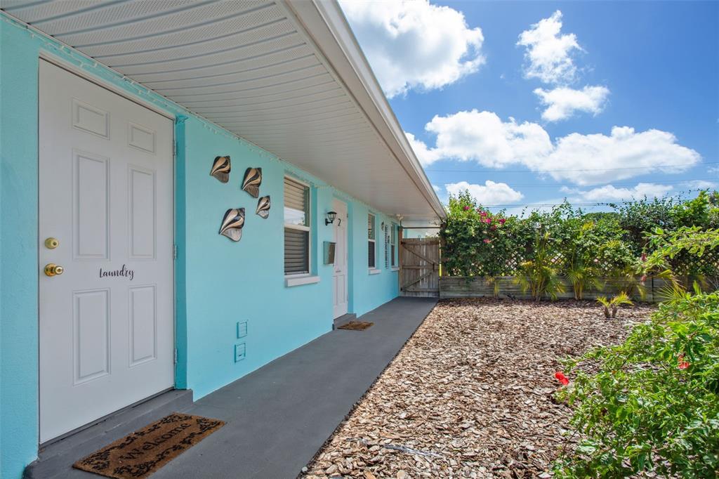 A light blue exterior wall features a laundry door and a walkway beside a yard — 1230 70TH STREET N, ST PETERSBURG, FL