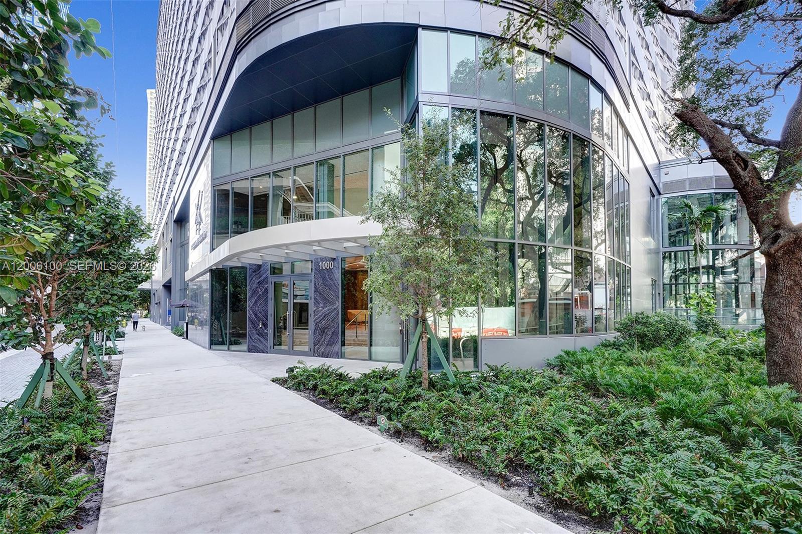 The exterior entrance of a modern high-rise building features glass walls and marble accents — 1000 Brickell Plaza, Miami FL 33131, MIAMI, FL