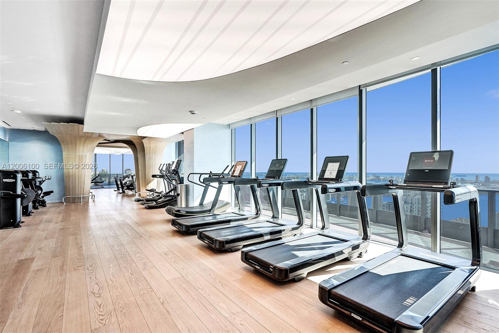 A modern gym features rows of treadmills facing floor-to-ceiling windows with a city view — 1000 Brickell Plaza, Miami FL 33131, MIAMI, FL