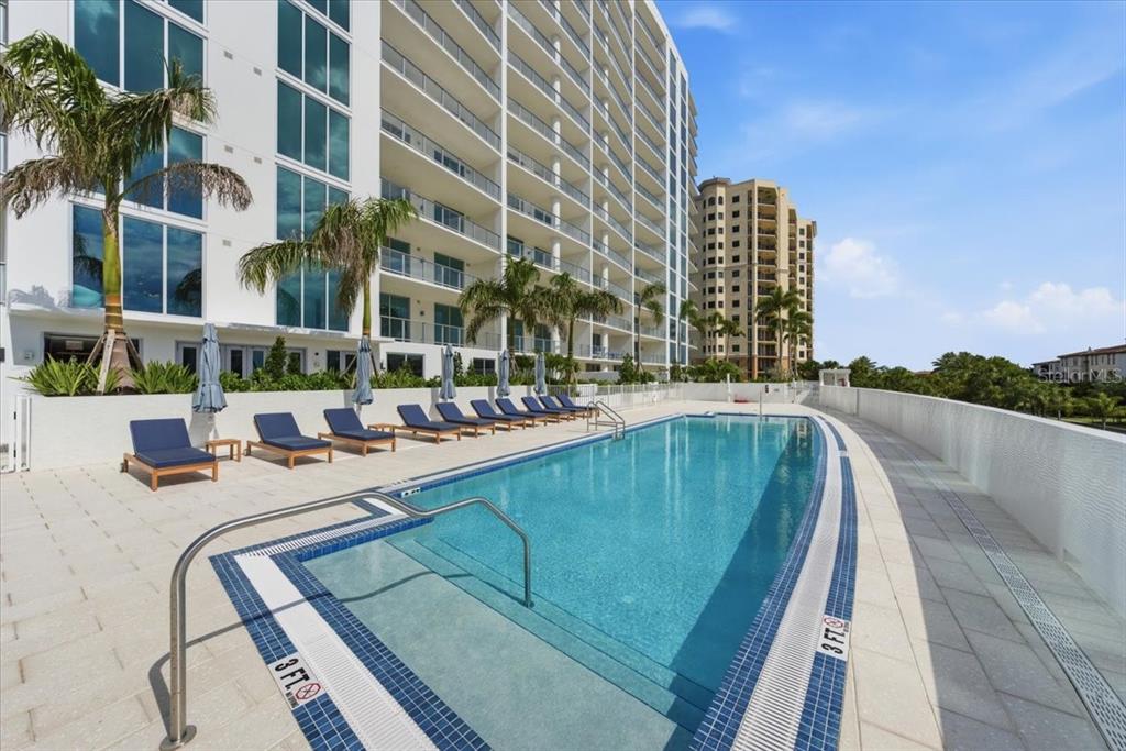 A rectangular swimming pool sits on a paved deck beside a tall residential building — 5713 BOWEN DANIEL DRIVE UNIT 402, TAMPA, FL